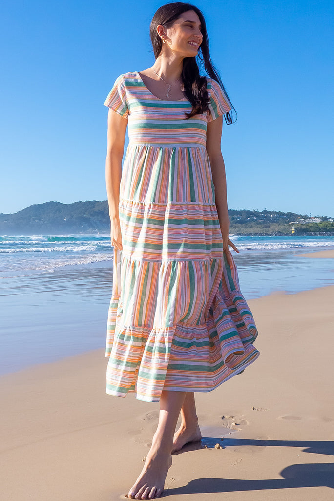 The Louisa Summer Sun Stripes Maxi Dress is a beautiful tiered maxi dress with green, white, orange and yellow stripes. This dress features a scooped neckline, adjustable waist tabs, side pockets and a wide tiered skirt. Made from a woven blend of cotton and polyester.