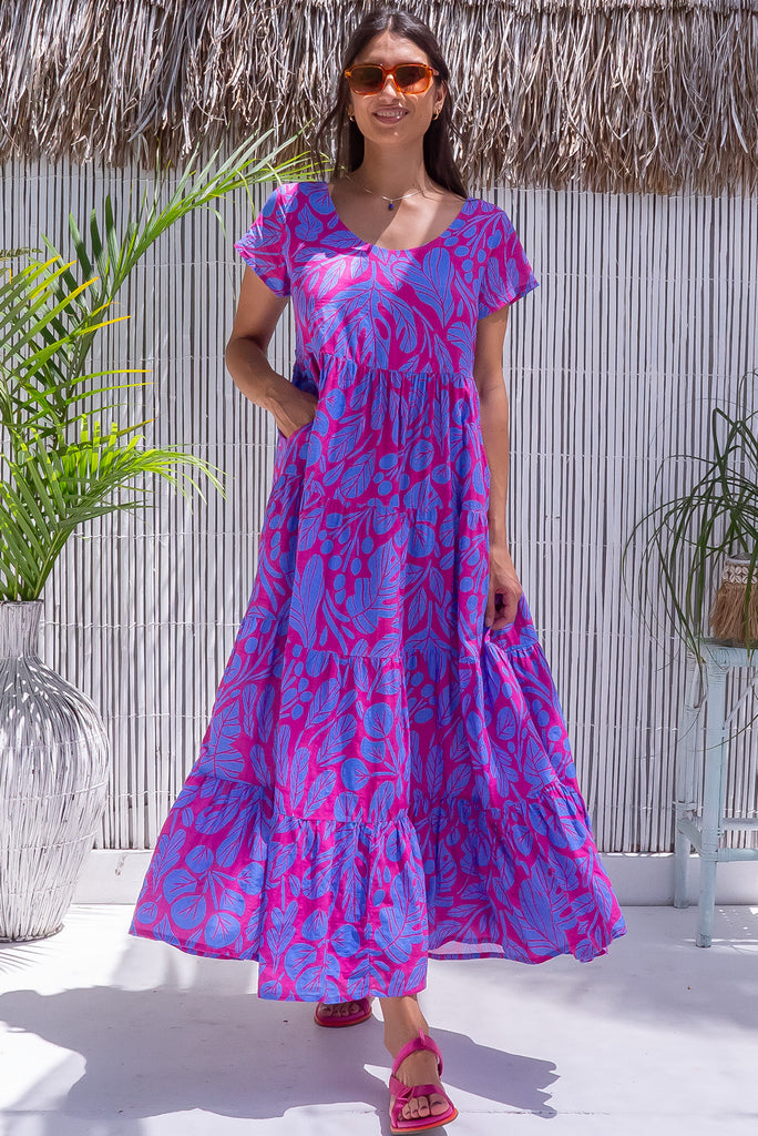 The Lucky Lulu Botany Bloom is a gorgeous hot pink dress with a tonal periwinkle botanical silhouette print. The dress features a wide neckline, was it tabs at the back and side pockets. Made from a woven blend of cotton and rayon.