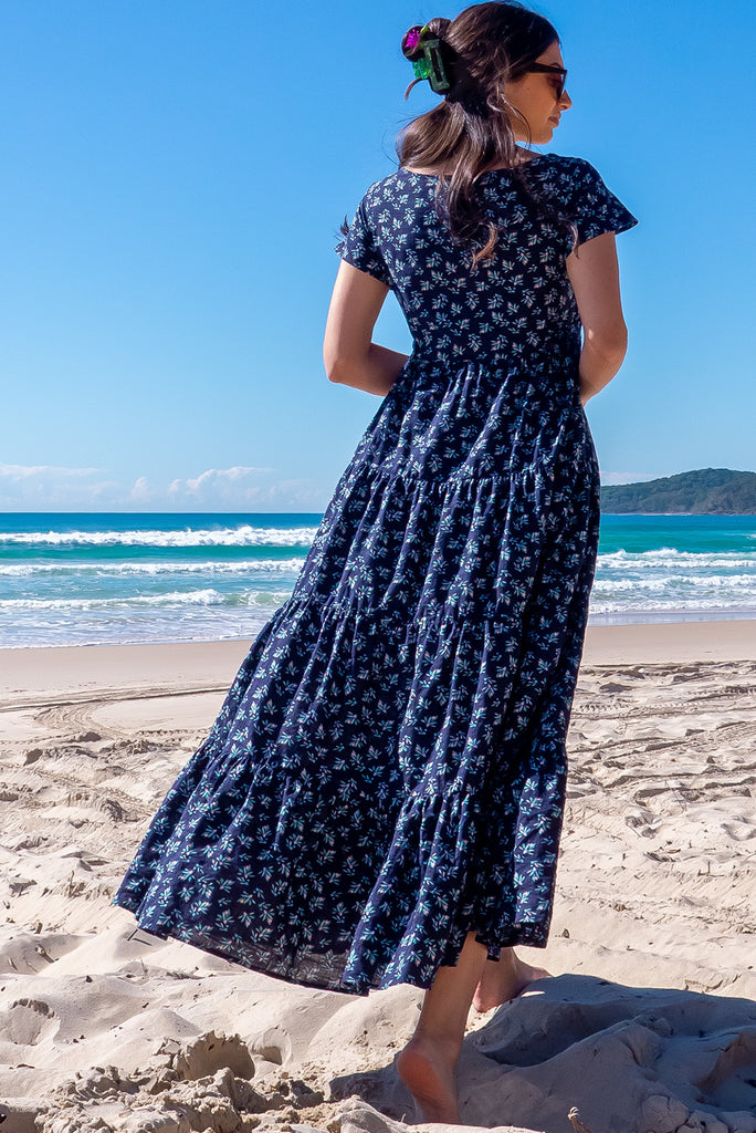 The Lucky Lulu Inky Sprinkle Maxi Dress is a beautiful tiered maxi dress with a navy blue base and small white floral print. This dress features a scooped neckline, adjustable waist tabs, side pockets and a wide tiered skirt. Made a woven blend of cotton and rayon.