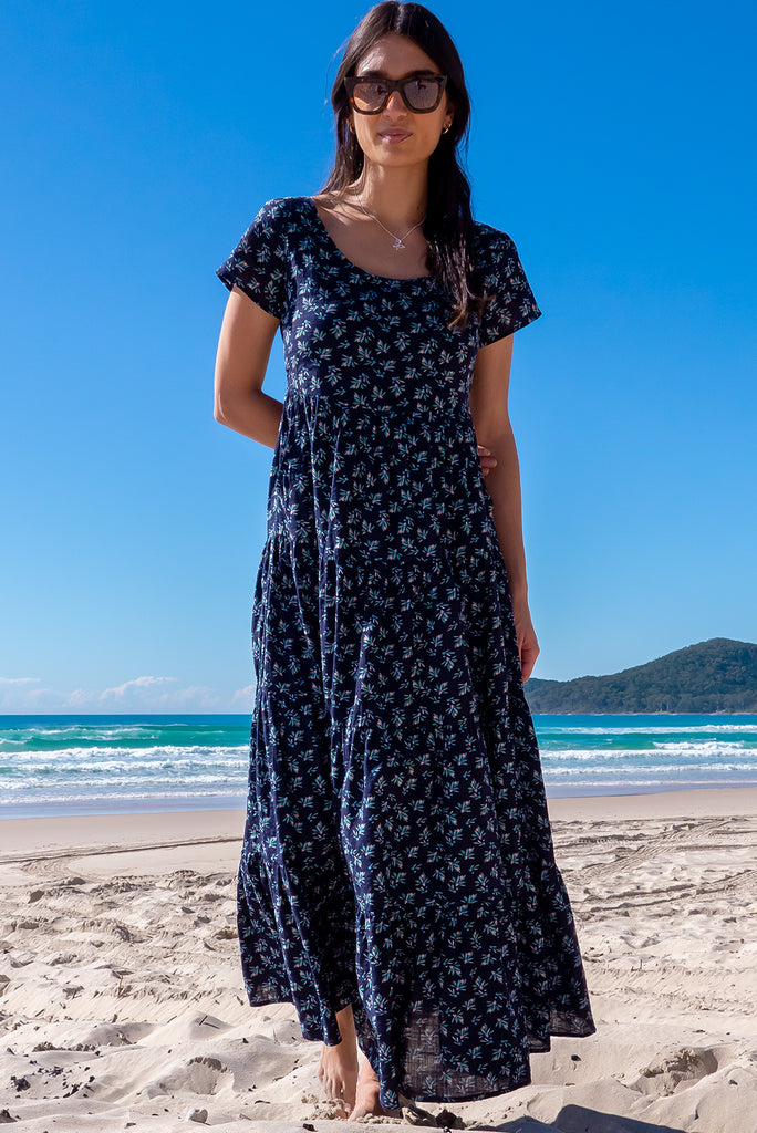 The Lucky Lulu Inky Sprinkle Maxi Dress is a beautiful tiered maxi dress with a navy blue base and small white floral print. This dress features a scooped neckline, adjustable waist tabs, side pockets and a wide tiered skirt. Made a woven blend of cotton and rayon.