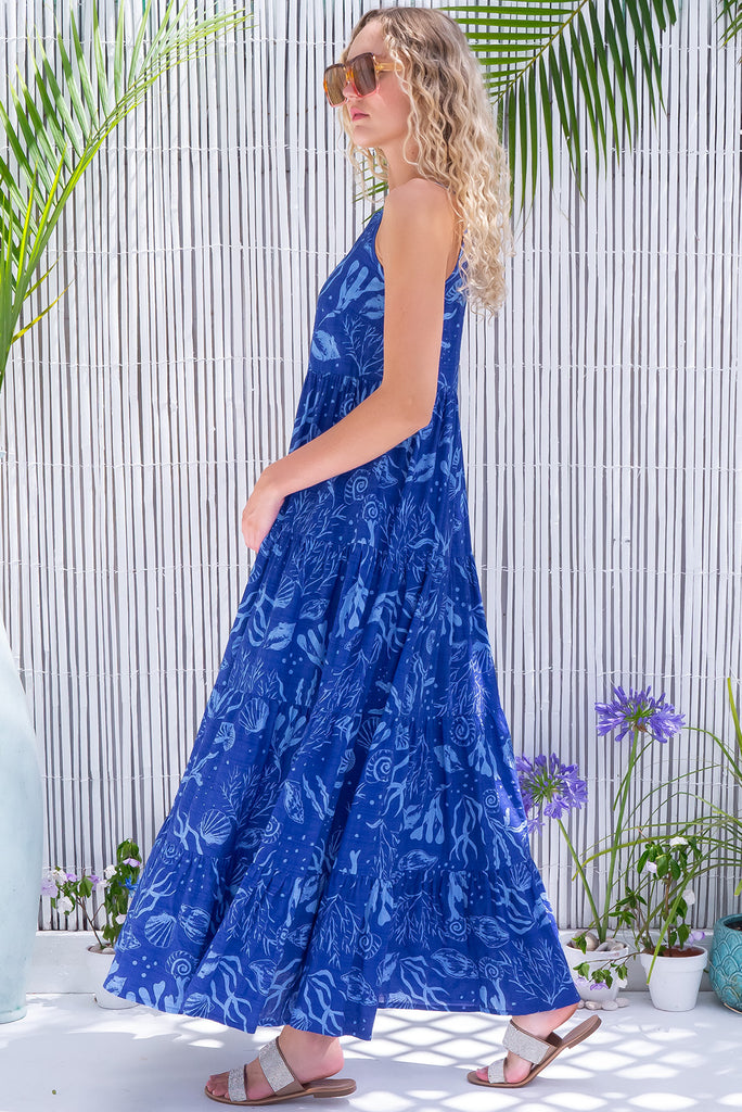 The Lulu Darling Ocean Deep Maxi Dress is a beautiful blue maxi dress with a pale blue seashell print. The dress features a high neckline, tiered skirting and side pockets, Made from a woven blend of cotton and rayon.