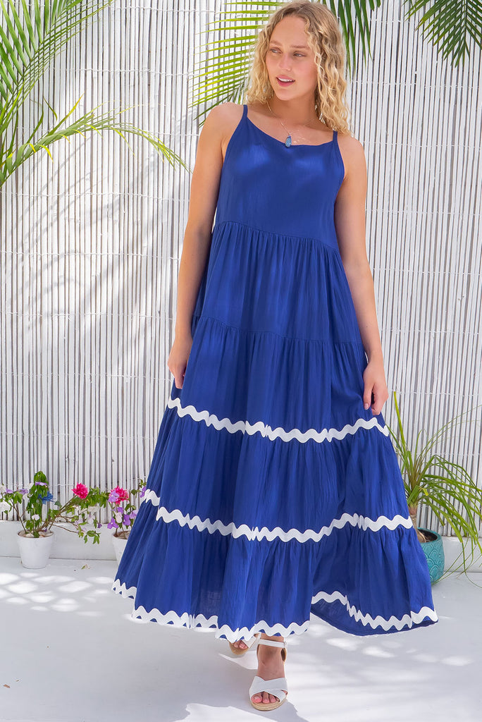 The Lulu Ric Rac Cobalt Maxi Dress is a beautiful blue maxi dress with a white oversized ric-rac braid feature. The maxi dress features a high neck, high cut under the arms, full tiered skirt falling from under bust, ric-rac on bottom three tiers, side pockets, and is made from woven cotton. 