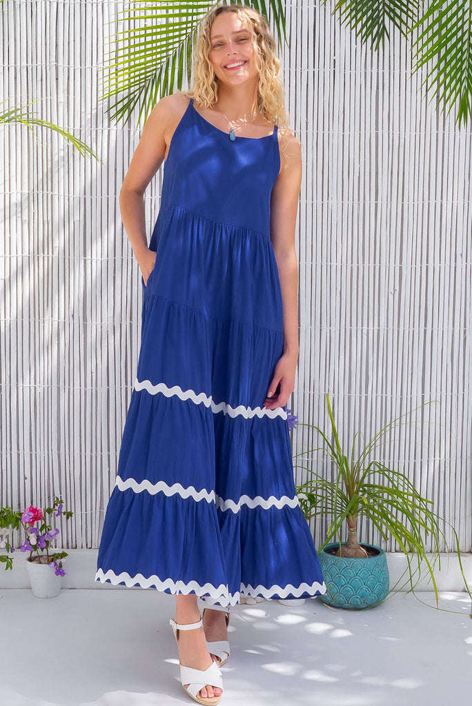 The Lulu Ric Rac Cobalt Maxi Dress is a beautiful blue maxi dress with a white oversized ric-rac braid feature. The maxi dress features a high neck, high cut under the arms, full tiered skirt falling from under bust, ric-rac on bottom three tiers, side pockets, and is made from woven cotton. 