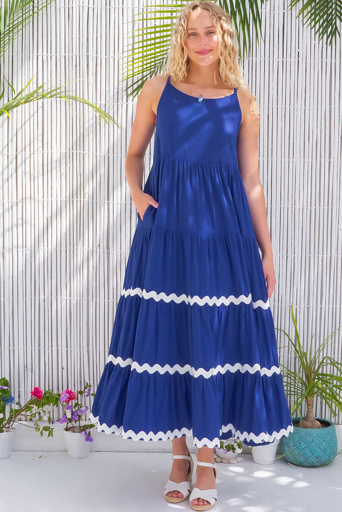 The Lulu Ric Rac Cobalt Maxi Dress is a beautiful blue maxi dress with a white oversized ric-rac braid feature. The maxi dress features a high neck, high cut under the arms, full tiered skirt falling from under bust, ric-rac on bottom three tiers, side pockets, and is made from woven cotton. 