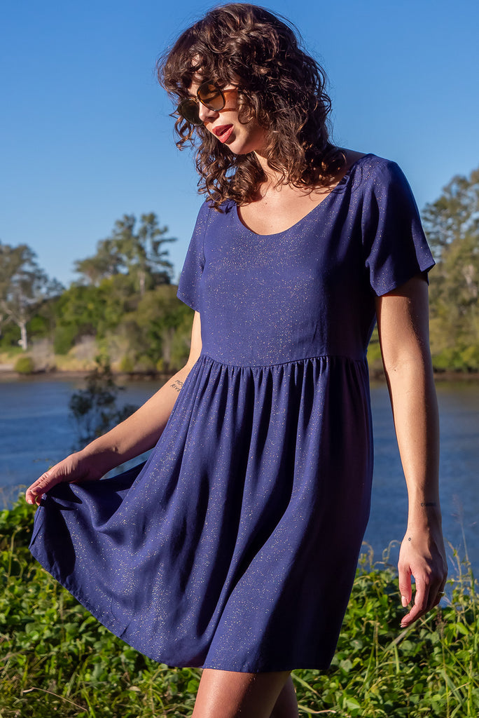 The Memento Ink Sparkle Mini Dress is is a beautiful navy blue dress with with a gold lurex shimmer all throughout. The mini dress features short sleeves, scooped neckline, and side pockets. Made from a woven blend of rayon, lurex, mulberry silk, and modal.