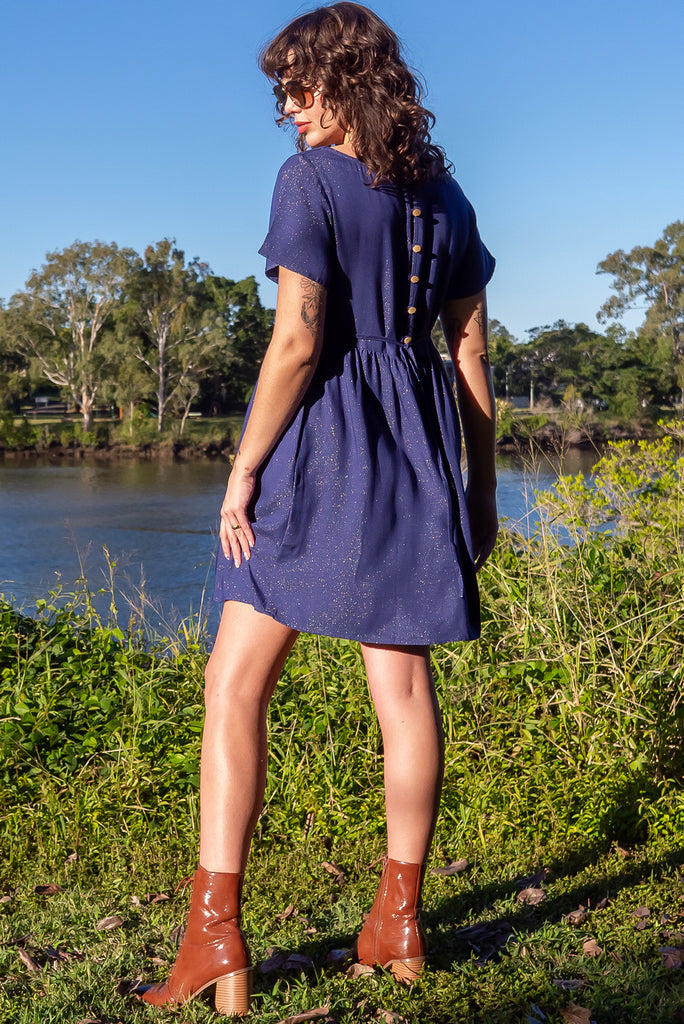 The Memento Ink Sparkle Mini Dress is is a beautiful navy blue dress with with a gold lurex shimmer all throughout. The mini dress features short sleeves, scooped neckline, and side pockets. Made from a woven blend of rayon, lurex, mulberry silk, and modal.
