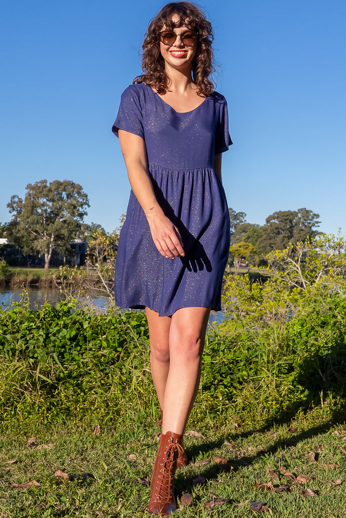 The Memento Ink Sparkle Mini Dress is is a beautiful navy blue dress with with a gold lurex shimmer all throughout. The mini dress features short sleeves, scooped neckline, and side pockets. Made from a woven blend of rayon, lurex, mulberry silk, and modal.