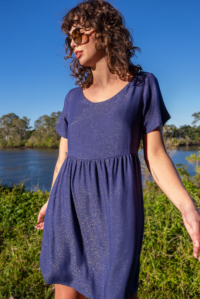 The Memento Ink Sparkle Mini Dress is is a beautiful navy blue dress with with a gold lurex shimmer all throughout. The mini dress features short sleeves, scooped neckline, and side pockets. Made from a woven blend of rayon, lurex, mulberry silk, and modal.
