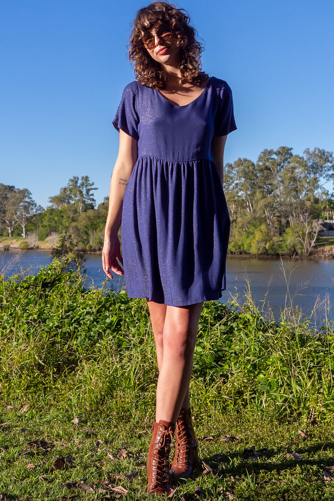 The Memento Ink Sparkle Mini Dress is is a beautiful navy blue dress with with a gold lurex shimmer all throughout. The mini dress features short sleeves, scooped neckline, and side pockets. Made from a woven blend of rayon, lurex, mulberry silk, and modal.