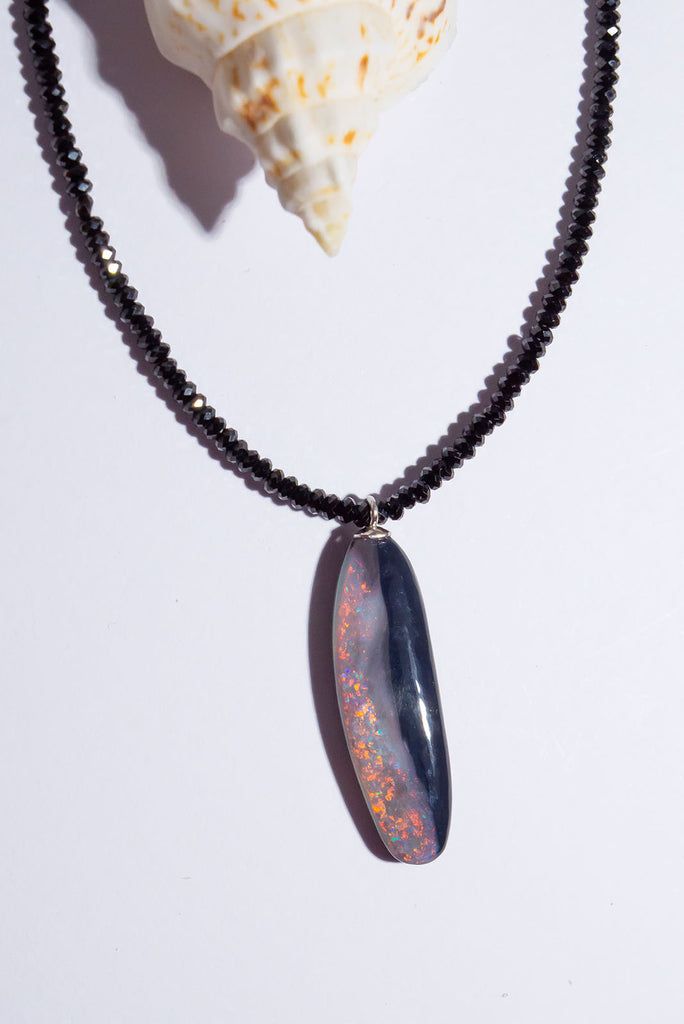 Discover the magic of Australian Black Opals. This incredibly chic necklace features a mesmerising organic cut opal with brilliant red, pink &amp; gold colour play.