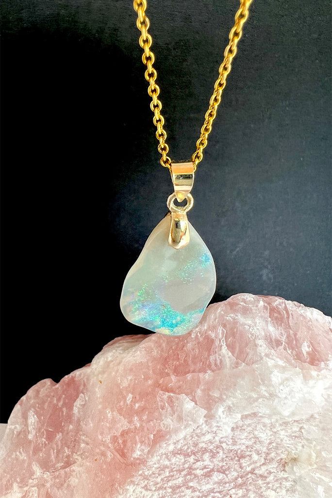 An absolutely stunning opal pendant featuring a soft sliver of Australian crystal opal cut and polished to show the wonderful colour that reveals itself underneath. The top of the stone is pale misty mauve, the base has bright flashes of green, blue and pinky orange. A rare one of a kind opal cut freeform with a highly polished undulating surface.