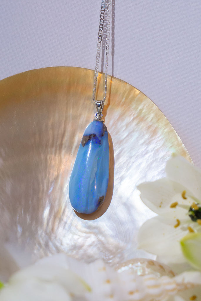 An Australian solid boulder opal pendant shaped into a droplet shape, with crystalline detail that reveals flashes of blue and mauve.