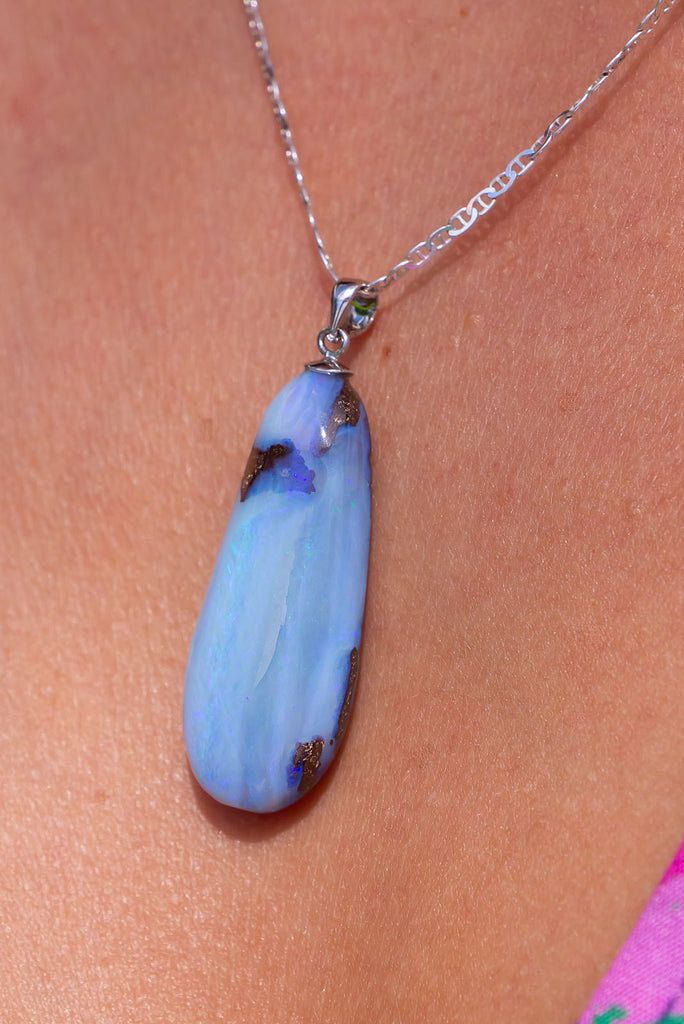 An Australian solid boulder opal pendant shaped into a droplet shape, with crystalline detail that reveals flashes of blue and mauve.