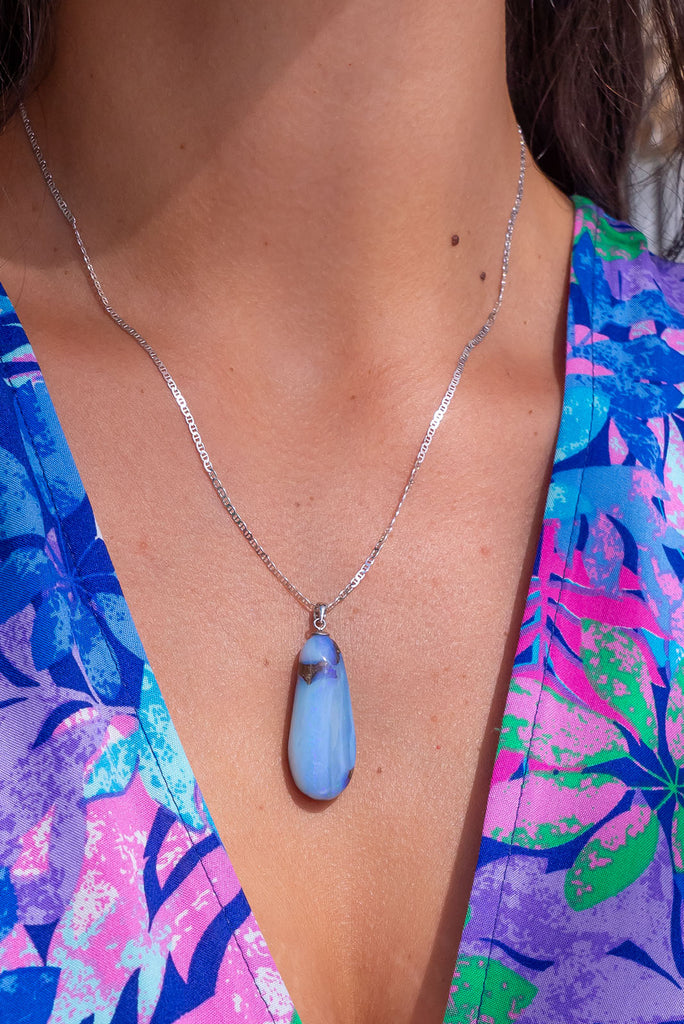 An Australian solid boulder opal pendant shaped into a droplet shape, with crystalline detail that reveals flashes of blue and mauve.