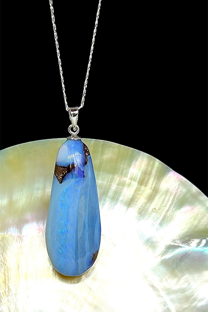 An Australian solid boulder opal pendant shaped into a droplet shape, with crystalline detail that reveals flashes of blue and mauve.
