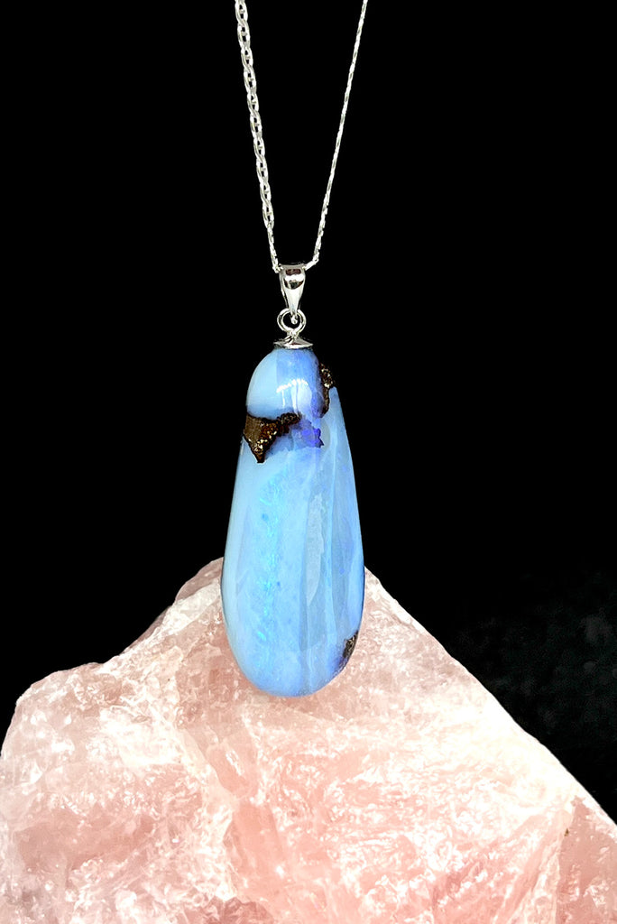 An Australian solid boulder opal pendant shaped into a droplet shape, with crystalline detail that reveals flashes of blue and mauve.