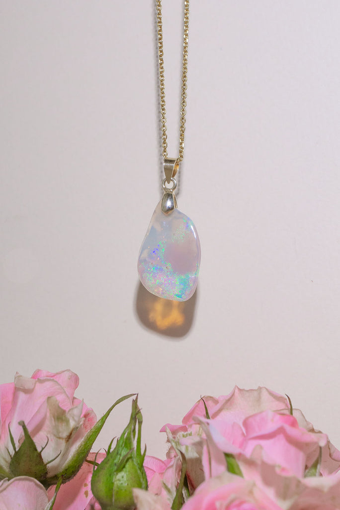 An absolutely stunning opal pendant featuring a soft sliver of Australian crystal opal cut and polished to show the wonderful colour that reveals itself underneath. The top of the stone is pale misty mauve, the base has bright flashes of green, blue and pinky orange. A rare one of a kind opal cut freeform with a highly polished undulating surface.