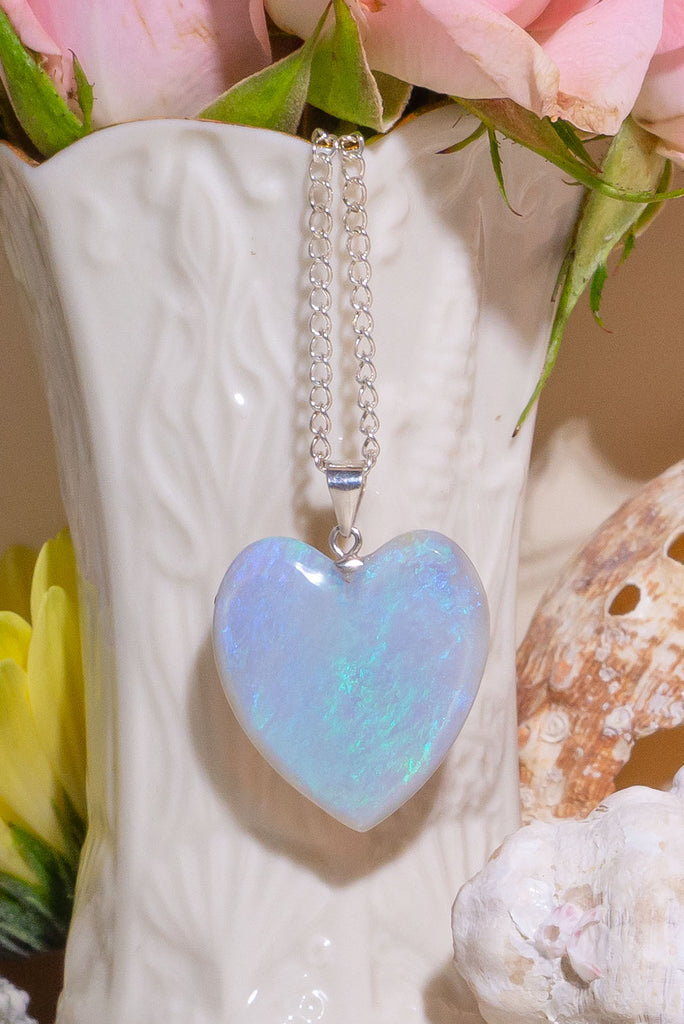 An Australian solid boulder opal pendant in a heart shape, misty mauve with very bright flashes of bright green and blue streaking across the whole stone.. This stone shows different colouration from different angles and is stunning in the sunlight.