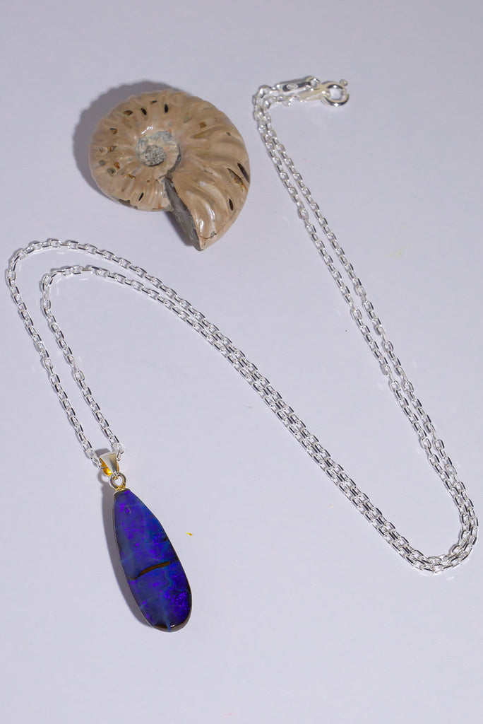 An elongated droplet shaped opal pendant, with pools of deep cobalt blue and a turquoise highlight, the ocean from above.