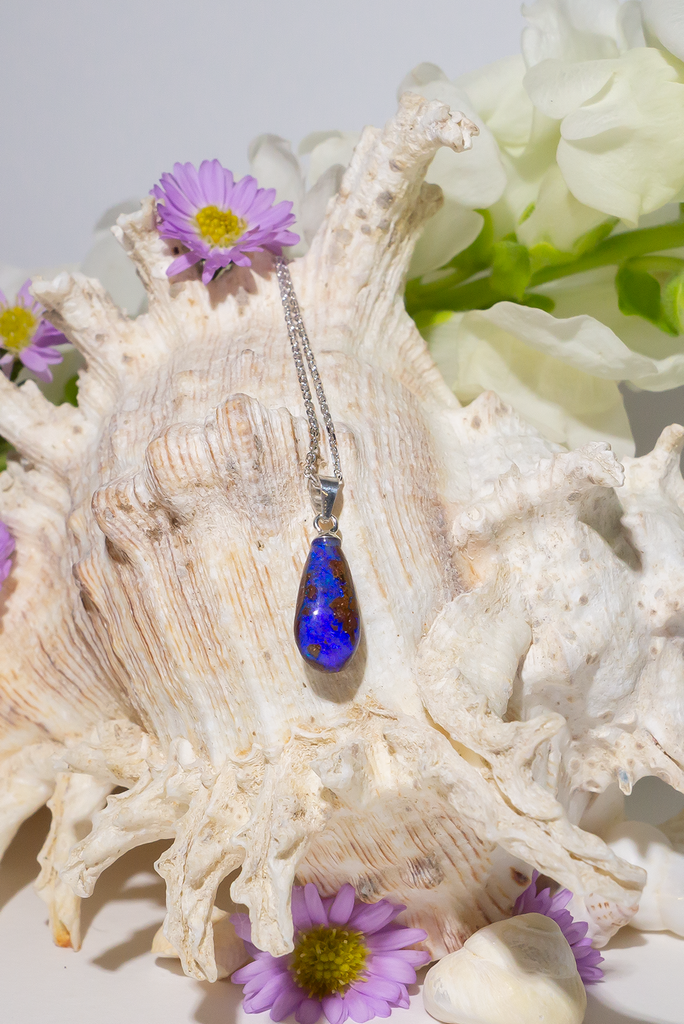 opal pendant is a small droplet shape, with deep blue purple crystal running down the stone, there is a landscape of dark islands
