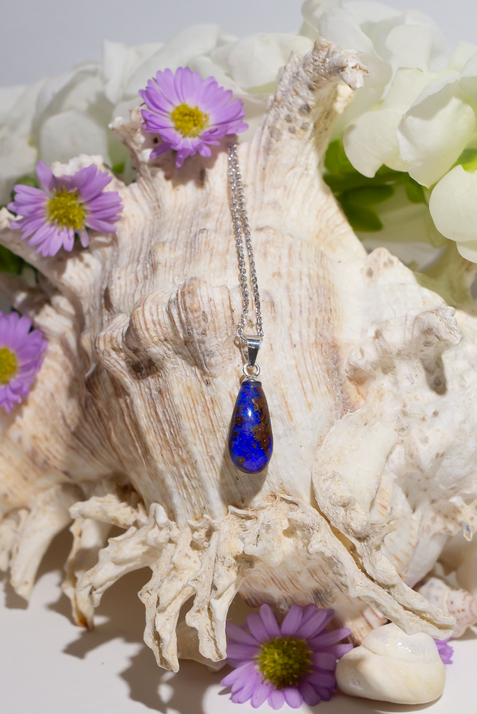 opal pendant is a small droplet shape, with deep blue purple crystal running down the stone, there is a landscape of dark islands