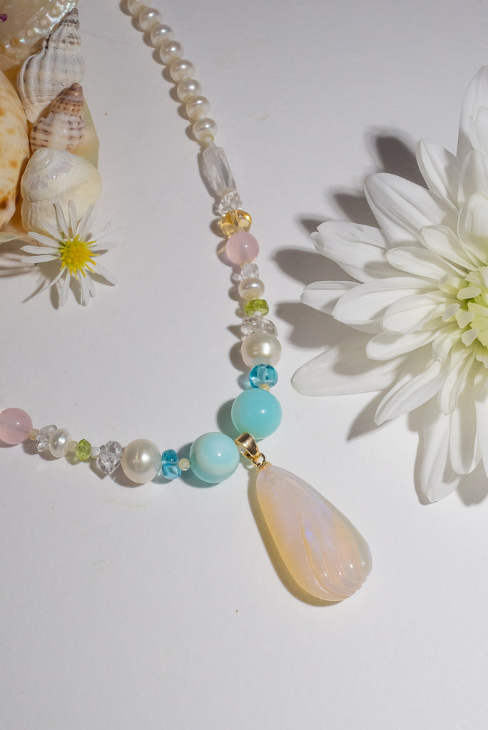 A beautiful creamy pink hand carved crystal opal with subtle flashes of green and blue, on a necklace of small lustrous pearls with gemstone highlights.