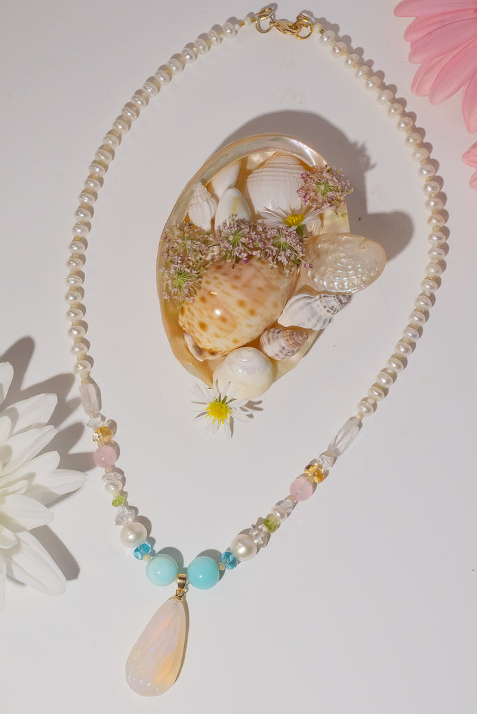 A beautiful creamy pink hand carved crystal opal with subtle flashes of green and blue, on a necklace of small lustrous pearls with gemstone highlights.