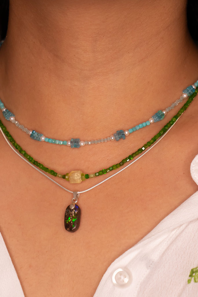This opal has a lovely green flash across the centre of the stone, it is cut into a rounded oval and shows the mark of the artist who cut and polished the stone. It has a river of blue running down one side.