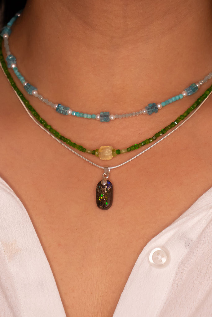 This opal has a lovely green flash across the centre of the stone, it is cut into a rounded oval and shows the mark of the artist who cut and polished the stone. It has a river of blue running down one side.