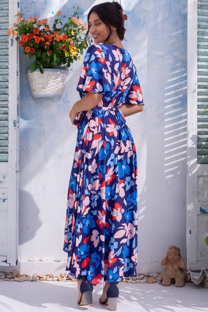 The Petal Blue Charm Maxi Wrap Dress is a beautiful blue maxi wrap dress with a large floral print. The dress features flutter sleeves, a functional wrap design, and side pockets. Made from 100% rayon.