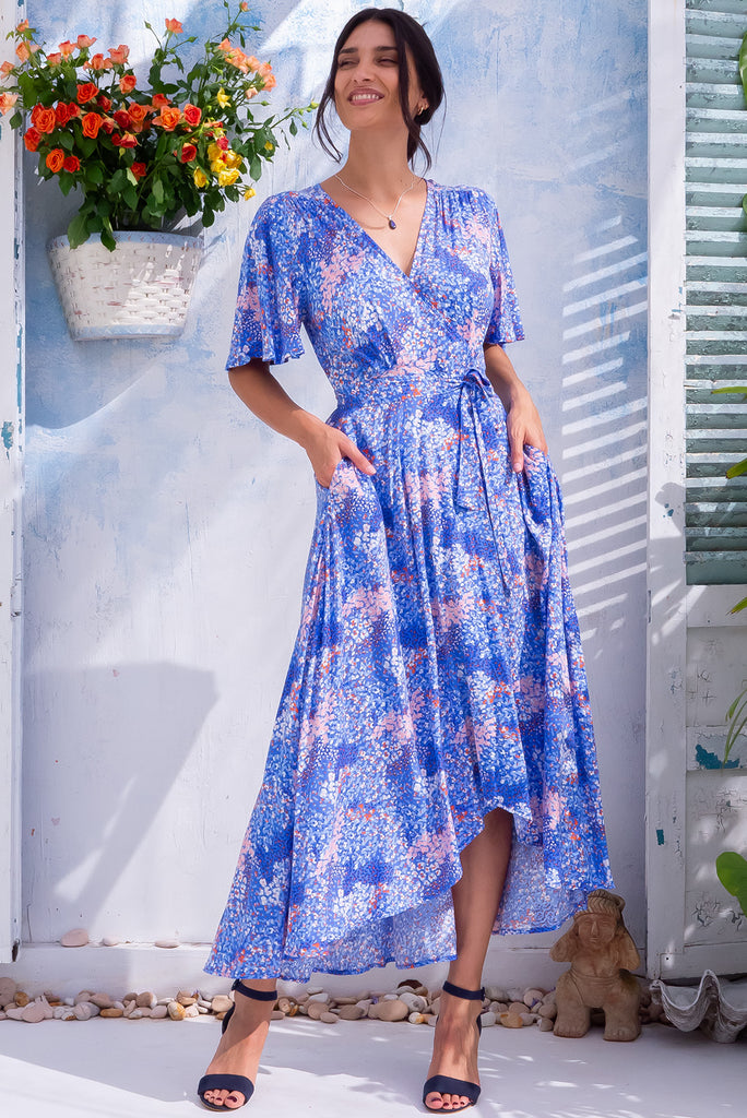 The Petal Confetti Blue Maxi Wrap Dress is a beautiful cornflower blue maxi dress with a pale pink and purple confetti style print all over. The dress features flutter sleeves, a functional wrap design, and side pockets. Made from 100% rayon. 
