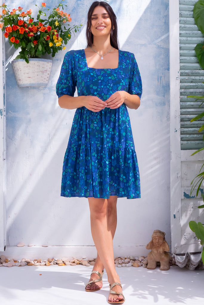 The Rosie Sea Shells Blue Mini Dress is a beautiful deep blue mini dress with a small cool-toned seashell print all over. The dress features a square neckline, puffy sleeves,  and adjustable waist tabs at the back. Made from a woven blend of cotton and rayon.