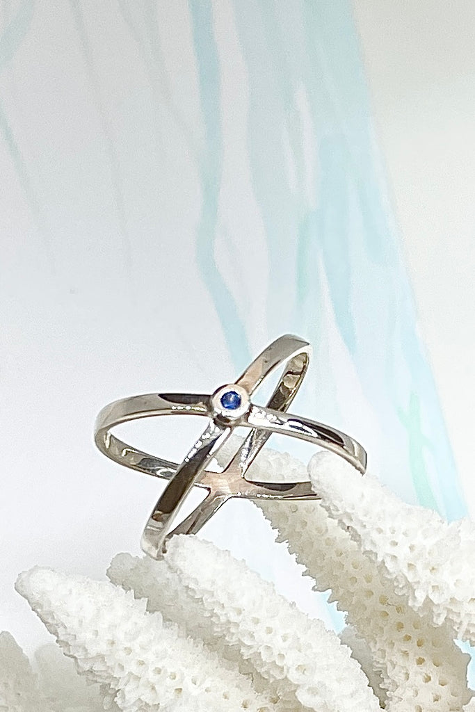 A simple Modern ring in minimal design in 925 silver. Features a small natural blue sapphire in the centre of two overlapping silver orbits.