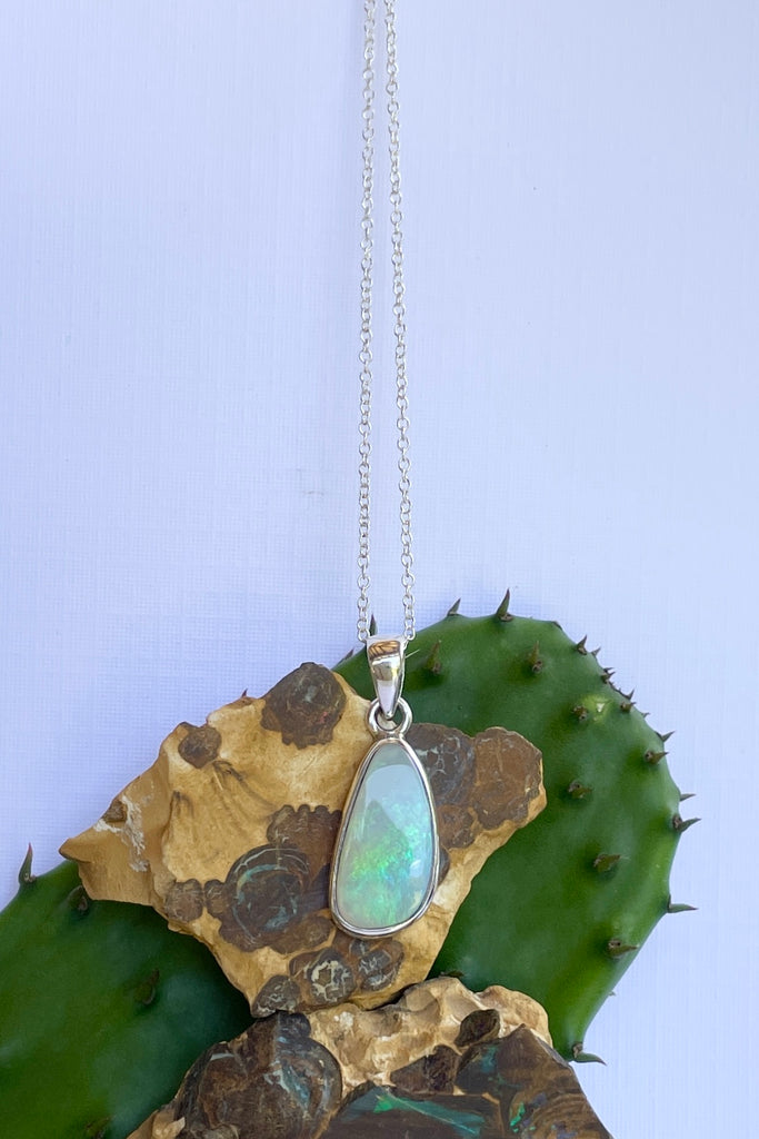 This Australian crystal opal pendant is shaped into an abstract shape with a polished frame surrounding it. The flashes of colour give one a glimpse into the past. 