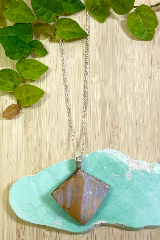 This opal is cut into a rough long triangle shape it has pale pinky blue opal flash with tiny flashes of green on the side. The face still shows some of the host rock from which it was cut.