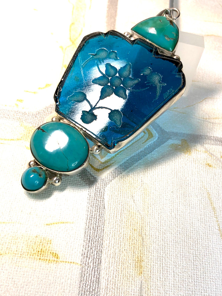 Echo Intaglio Blue Pendant is a mystical and historical pendant featuring Unsymmetrical cut turquoise glass intaglio and each piece has been set in silver.