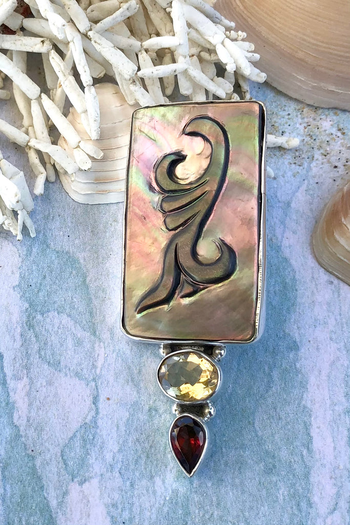 The Echo Pendant Keeper in 925 silver is a substantial piece, there is an exotic foliate design hand carved onto black lip Mother of Pearl. At the base is an oval citrine and a tear drop garnet. 