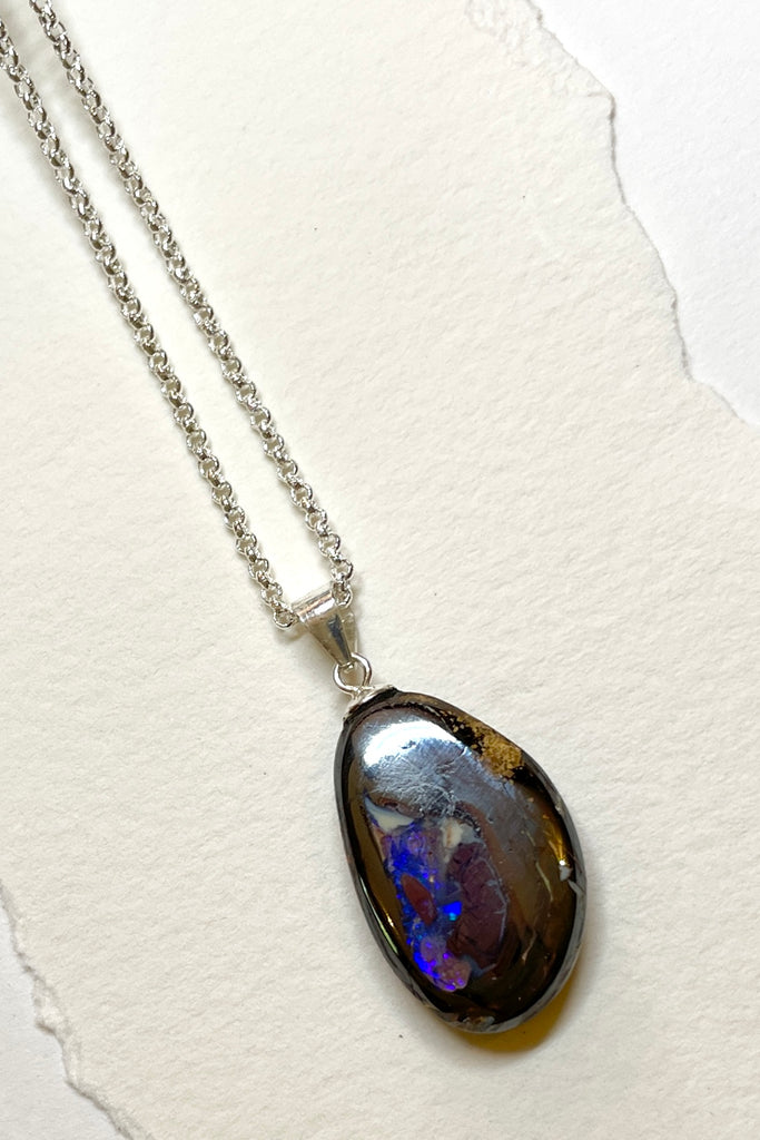 A lovely oval free form cut natural piece of Boulder Opal with interesting patterns and bright blue and crystal down one side. Australian Opal.
