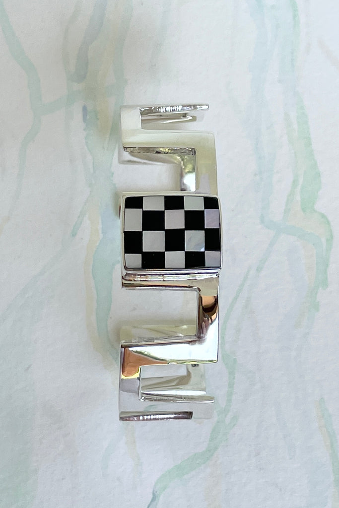 Very cool and sophisticated, this 925 silver cuff bracelet rocks the modern retro cool. In a square geometric design featuring a centre square inlaid with mother of pearl and black enamel,