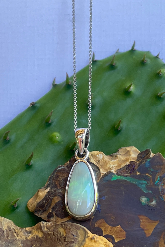 This Australian crystal opal pendant is shaped into an abstract shape with a polished frame surrounding it. The flashes of colour give one a glimpse into the past. 