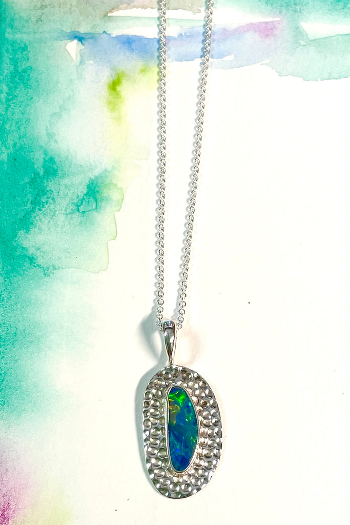 Australian opal pendant is shaped into an abstract shape with a polished frame surrounding it. The flashes of colour in the opal give one a glimpse into the past. 