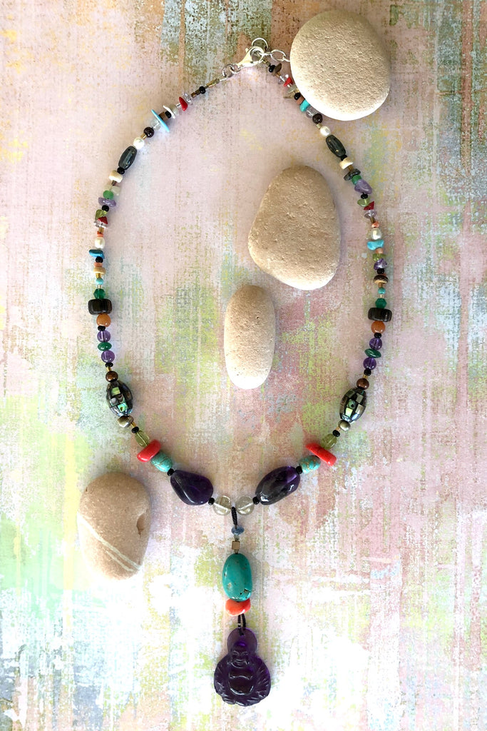 The elegant centre piece of this divine necklace is a mystical Deity carved in clear purple Amethyst and other stones on the chain include Peridot, Bad Howlite, Paua shell mosaic bead, green onyx, Carnelian, Amethyst, Golden Rutile Crystal and wood.