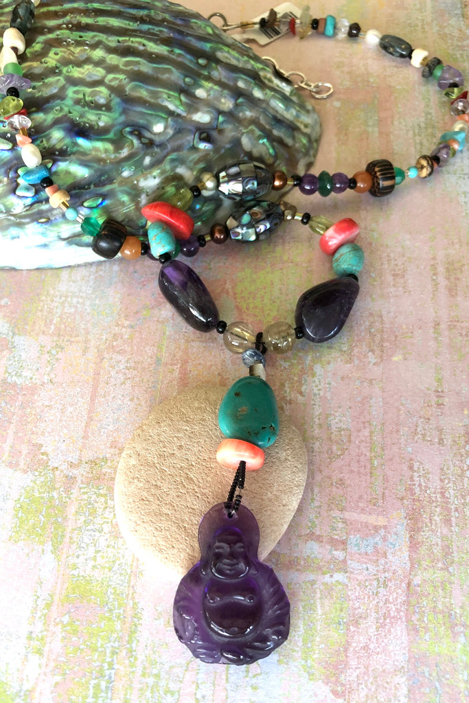 The elegant centre piece of this divine necklace is a mystical Deity carved in clear purple Amethyst and other stones on the chain include Peridot, Bad Howlite, Paua shell mosaic bead, green onyx, Carnelian, Amethyst, Golden Rutile Crystal and wood.