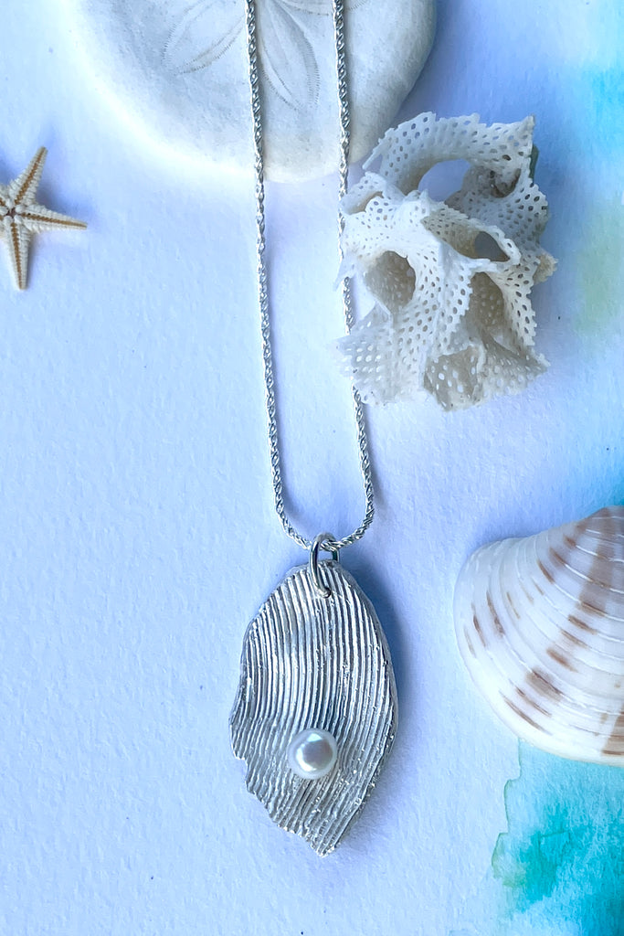 The pendant is solid silver, it is cast from the surface of a Pippi shell, and designed to carry the pearl bubble on the waves reaching the shore.
