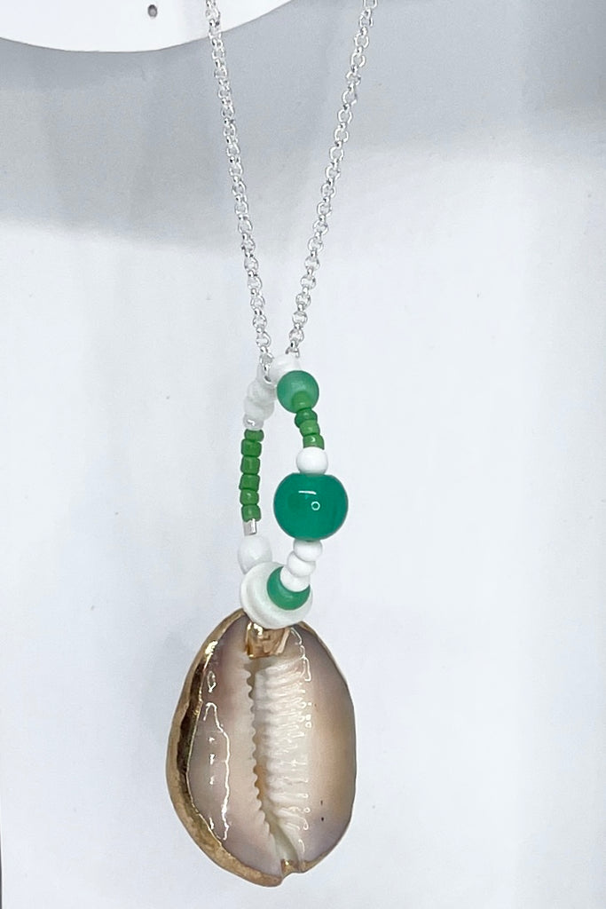 A pendant keepsake made with a cowrie shell which hangs from a circlet of simple green and white village beads. Then suspended from a chain.