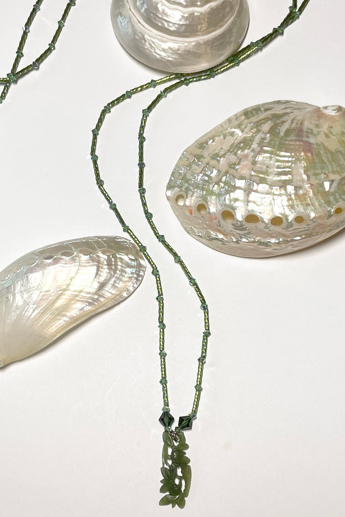 necklace is opera length and can be worn long or doubled to be shorter. Crystal glass bugle beads and green Swarovski crystals. The centre is a pendant of beautifully carved foliage in greenstone jade.