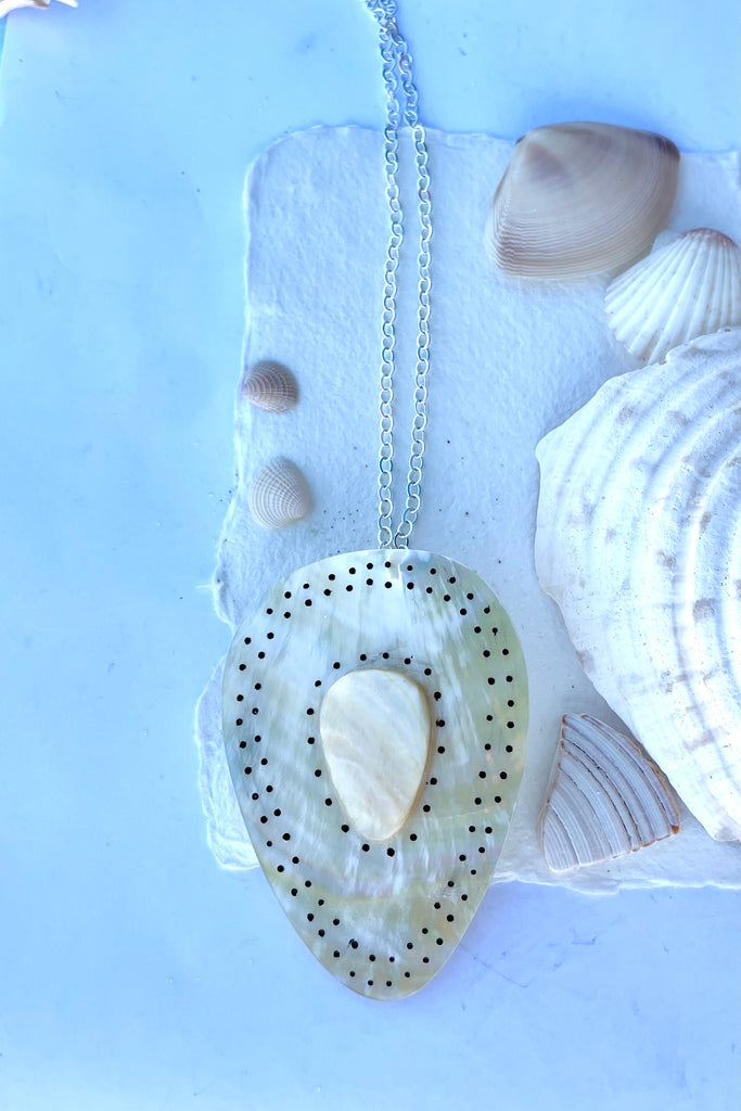 Beautiful golden Mother of Pearl shell pendant cut into a strong tribal shape, it has inlaid spots that give it the feeling of strength