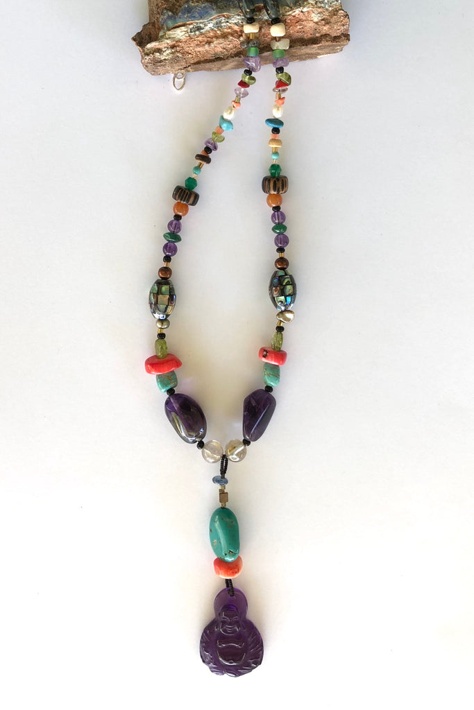 The elegant centre piece of this divine necklace is a mystical Deity carved in clear purple Amethyst and other stones on the chain include Peridot, Bad Howlite, Paua shell mosaic bead, green onyx, Carnelian, Amethyst, Golden Rutile Crystal and wood.