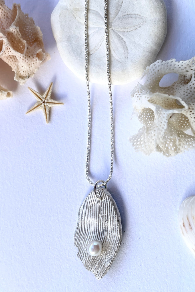 The pendant is solid silver, it is cast from the surface of a Pippi shell, and designed to carry the pearl bubble on the waves reaching the shore.