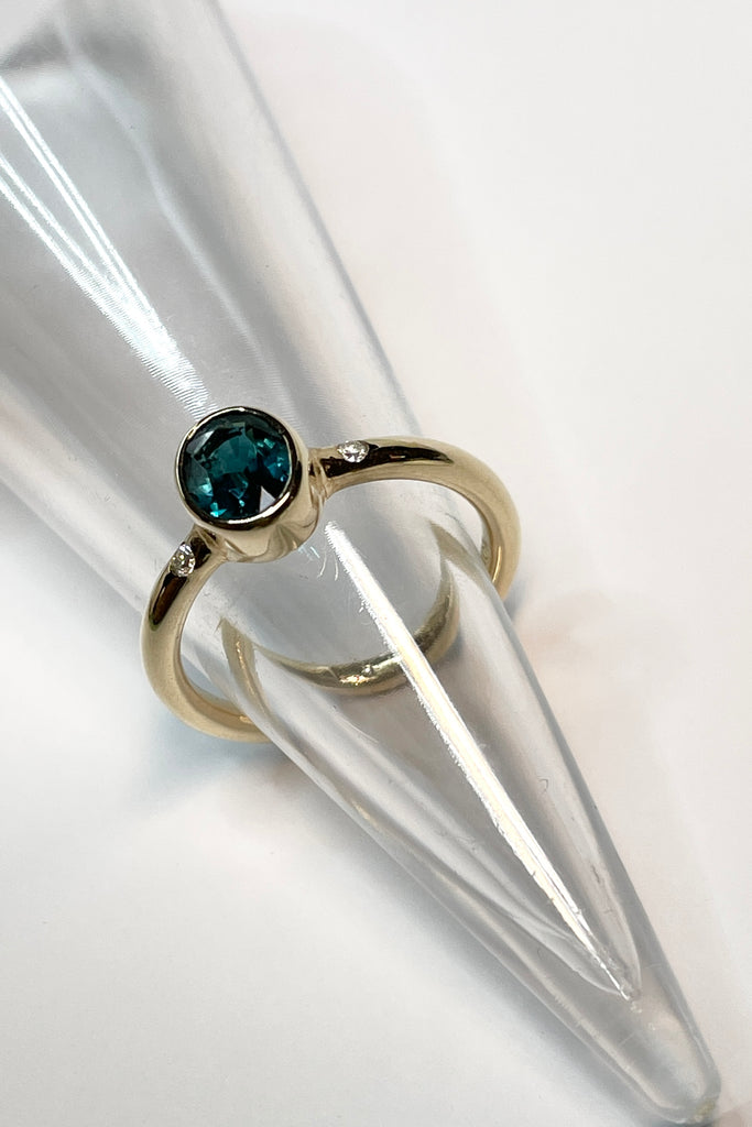 A beautiful simple ring designed to complement the lovely natural teal blue tourmaline gemstone set into the ring. The shank of the ring has a diamond on each side of the centre stone.